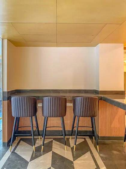 A close-up of the bar seating in the Bhopal hotel. The design features stylish bar stools with brass-tipped legs and a bold geometric floor pattern, adding a touch of art deco glamour.