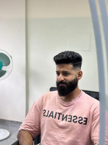A mirror view of a client with a high fade and a full beard.