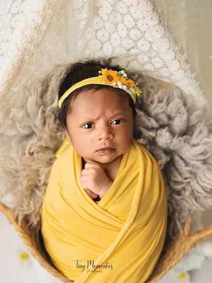 This little one is wide awake and full of expression. The bright yellow wrap and daisy props create a cheerful and sunny atmosphere for the photoshoot.