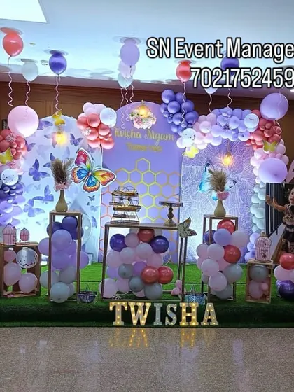 A grand butterfly-themed stage decoration. This elaborate setup features large butterfly wing props, a custom backdrop, and beautiful balloon arrangements on a green turf floor.