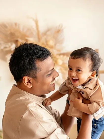 A father and son share a laugh. The dad lifts his son, and the boy's happy expression is a perfect reflection of the fun they're having together.