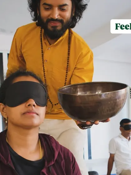 A blindfolded participant feeling the vibrations of a singing bowl up close.