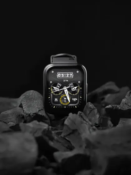 A product shot of a realme watch on a bed of charcoal, using the contrast between the sleek black watch and the rough texture of the coal.
