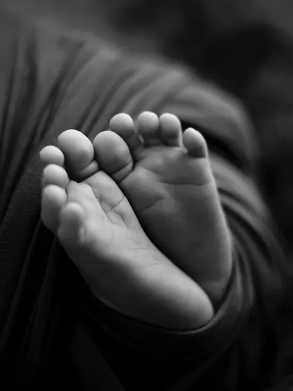 A close-up of a newborn's tiny feet, captured in black and white to highlight the wrinkles and details.