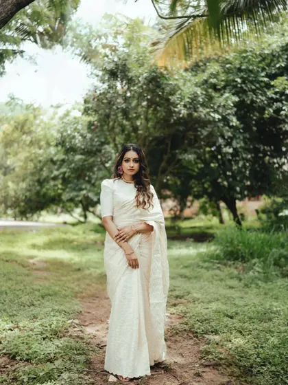 A full-length portrait showcasing the grace of a traditional Onam look. The serene, natural background allows the classic beauty of the Kerala saree to stand out.