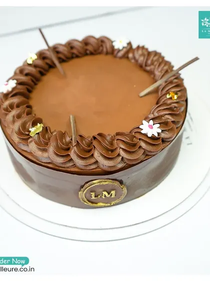 My signature Chocolate Truffle cake is pure indulgence. It features a silky smooth ganache, a border of piped chocolate cream, and is simply decorated with chocolate sticks and tiny flowers, letting the rich flavor shine.