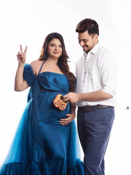 A fun and happy couple's portrait. The mom-to-be makes a peace sign while her partner holds the baby shoes, capturing a moment of pure joy and excitement.