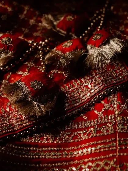 A close-up of the rich, red fabric and intricate tassels of a bridal lehenga. This detail shot highlights the craftsmanship and beauty of the bride's attire.