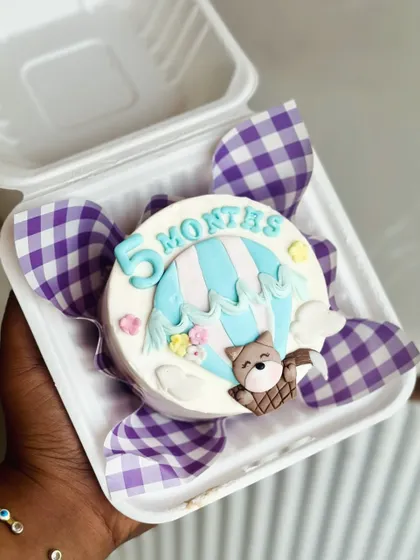 This five month bento cake is ready for an adventure, featuring a hot air balloon and a cute teddy bear. It's a small cake that tells a big story.
