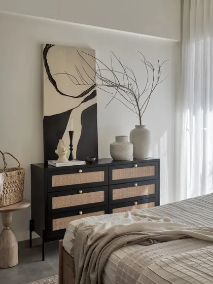 A chest of drawers in a sophisticated black matte PU finish with cane accents adds a striking contrast to this bedroom’s subtle beige tones, providing both storage and style.