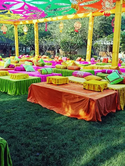A wide view of a colorful Mehendi setup with low seating and a vibrant canopy, designed for a large and lively celebration.