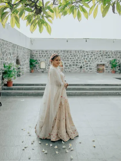 A beautiful, full-length portrait of the bride at Fort Jadhavgadh. The historic stone walls and the scattering of petals on the ground add a rustic and romantic charm.