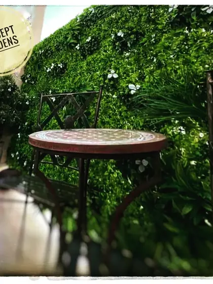 A simple cafe-style seating arrangement set against a backdrop of our artificial green wall with small white flowers. This creates a charming and maintenance-free outdoor cafe feel.