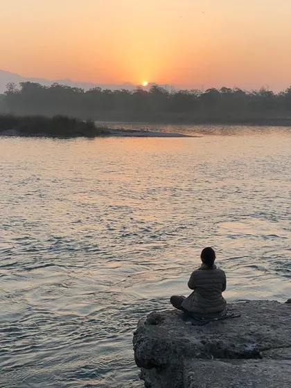 Meditating by the river at sunrise. The flowing water and rising sun create a powerful and serene environment for practice.