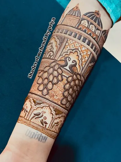 The left arm of the engagement mehendi, with a focus on a beautiful peacock and palace (jharokha) design.