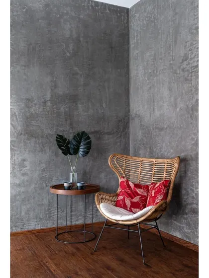 A quiet corner in Nataraj House. The raw cement-finished walls provide a perfect, textured backdrop for a simple cane chair, embodying the home's earthy theme.