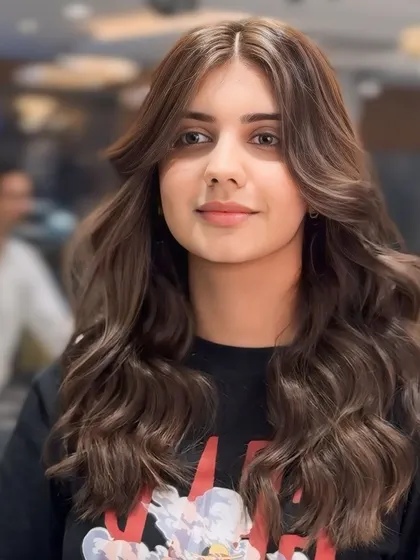 A beautiful portrait of our ash brown hair color. Styled with soft waves and a center part, this look features face-framing layers that highlight the client's features.