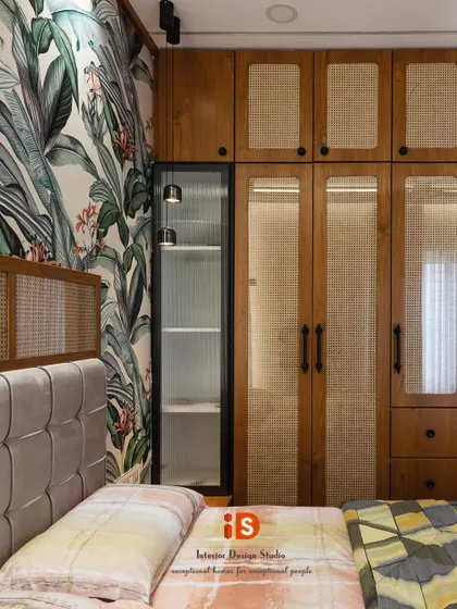 This bedroom design uses natural materials like cane and wood to create a warm, earthy feel. The wardrobe features cane-paneled doors, complementing the tropical wallpaper and upholstered headboard.