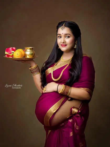 A classic portrait inspired by the paintings of Raja Ravi Varma. The mother-to-be, in a beautiful magenta saree, holds a traditional offering plate, embodying grace and heritage.