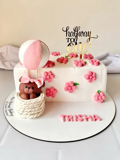 A 'halfway to one' cake for a six-month celebration. This adorable cake features a teddy bear in a hot air balloon, surrounded by pink flowers.