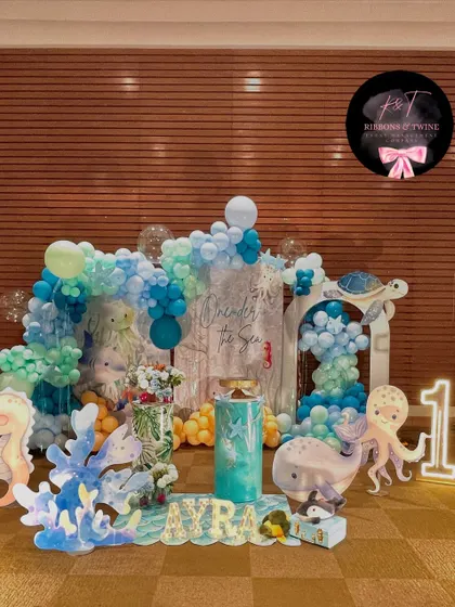 An enchanting 'One-der the Sea' first birthday celebration for baby Ayra. This full view showcases the cohesive underwater theme with blue balloon waves, adorable sea creature cutouts, and personalized marquee letters.