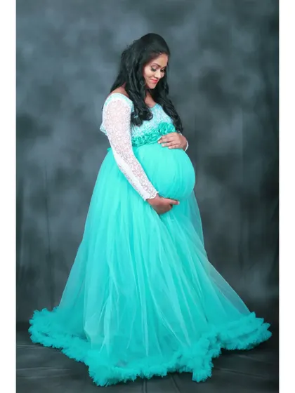 A classic pose cradling the baby bump in our cyan and white gown. The color stands out beautifully against the dark, textured backdrop.