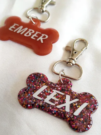 These custom pet tags for 'Ember' and 'Lexi' show off different styles. One is a solid color, while the other is full of fun, multi-colored glitter.