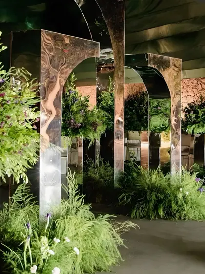 An installation of mirrored arches surrounded by ferns and greenery. The reflections create an illusion of a larger, more immersive space, adding a touch of modern magic to the decor.