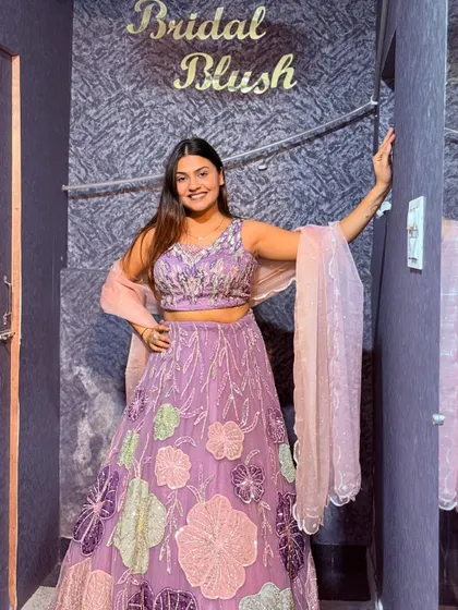 A happy client posing in our lavender lehenga with colorful floral appliqué work.