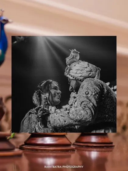 A creative black and white shot of the Varmala ceremony, framed by a peacock figurine.