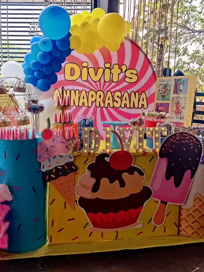 A colorful and sweet candy-themed Annaprasana ceremony. The decor is filled with giant ice cream cone and cupcake cutouts, a candy-striped backdrop, and bright balloon clusters.