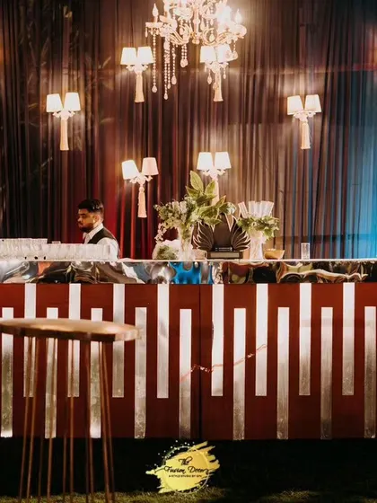 This modern bar design combines sleek metallic lines with warm, ambient lighting from wall sconces and chandeliers. It’s a stylish and functional centerpiece for any cocktail or sangeet night.