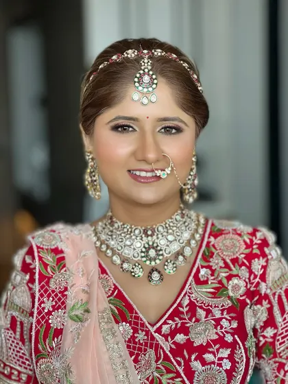 A stunning portrait of a bride in a red lehenga. The makeup is classic and polished, with a focus on flawless skin and defined eyes.