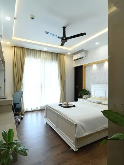 This serene bedroom features a beautiful wallpapered arch panel behind the bed and a stunning aristo wardrobe with lacquered glass. A multipurpose unit combines storage, a study desk, and a dresser.