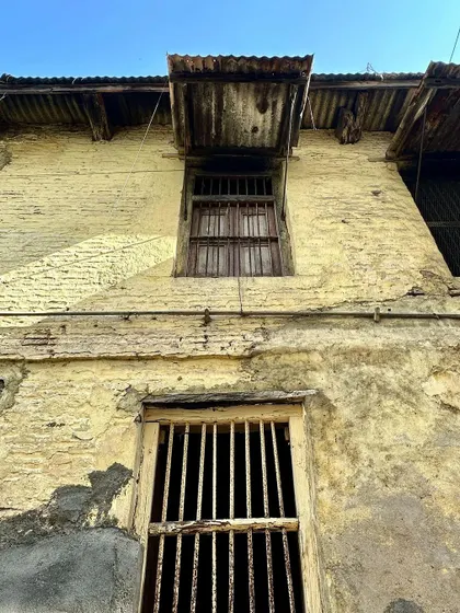 A view looking up at the weathered facade and windows of a traditional building in Vadodara. The simple, functional design of the window shutters and awnings is a response to the local climate.