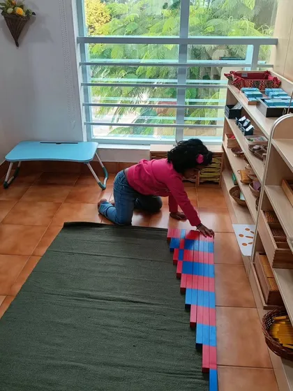 A child works with the red and blue number rods, a material used to teach counting and quantity. By arranging them, she is visually and physically grasping the concept of ascending numbers.