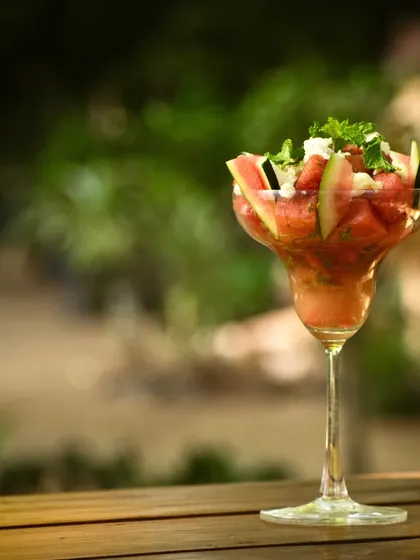 A watermelon and feta salad served in a cocktail glass. This creative presentation is captured against a soft, green background, emphasizing its freshness and suitability for a summer menu.