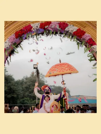 A joyous moment as the couple is showered with petals during their grand entrance, seated in a palanquin under a decorative umbrella.