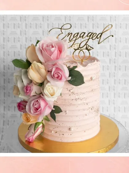 A beautiful engagement cake with a textured buttercream finish, a cascade of fresh roses, and a custom 'Engaged' topper. It’s a perfect blend of rustic charm and floral elegance.