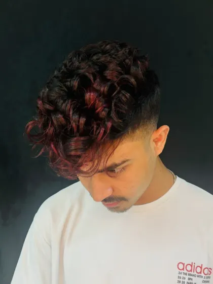 A modern men's style featuring a sharp fade and textured curls with fiery red tips. This look combines advanced cutting and creative coloring skills.