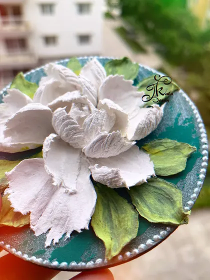 A simple and elegant fridge magnet featuring a single white gardenia on a dark green background. The contrast makes the white petals, sculpted with lots of texture, really stand out.