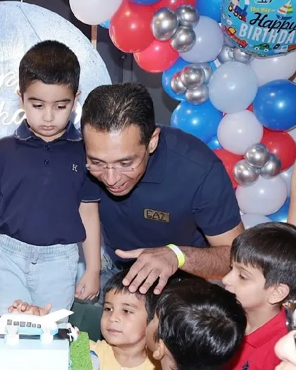 The family helps the birthday boy cut his airplane-themed cake as his friends watch on.
