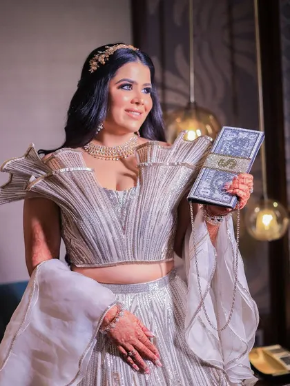 A stunning portrait of the bride in her modern, structured lehenga, holding a unique money-themed clutch. We love capturing the personal style and unique details of our brides.