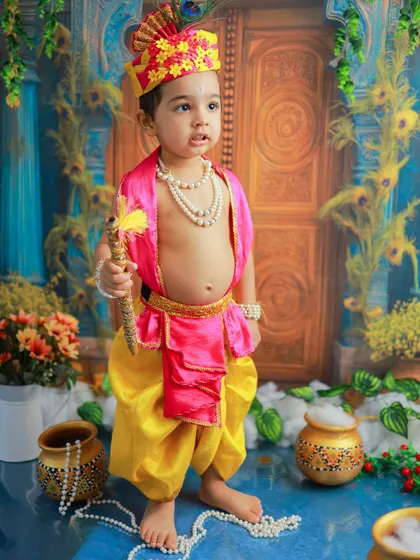 A full-length portrait of our little Krishna, standing tall with his flute. The detailed costume and backdrop create a majestic and divine atmosphere.