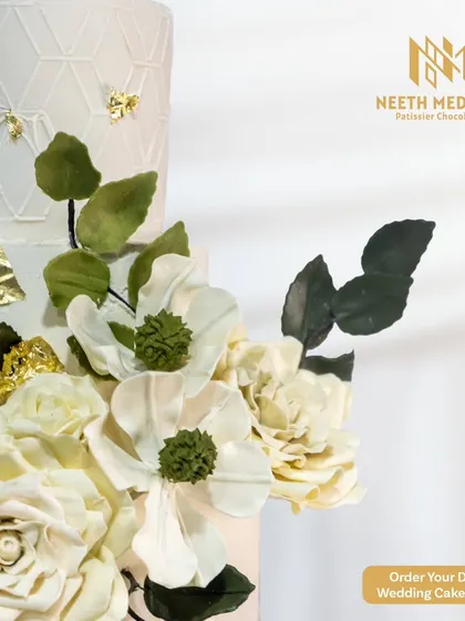 A detailed shot of the handcrafted white sugar flowers on our elegant four-tiered wedding cake. The delicate petals and gold leaf accents showcase the artistry and attention to detail in my work.