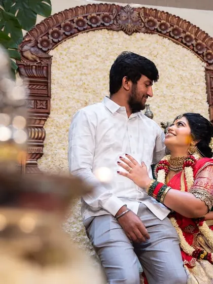 A sweet, candid moment between the couple during a traditional function, framed by a blurred foreground element for an artistic touch.