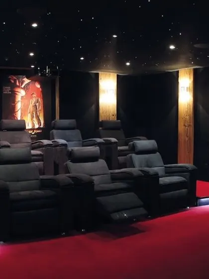 This modern cinema room features a bold red carpet, tiered black leather recliners, and framed movie posters for a personalized touch. The layout is optimized for clear sightlines and balanced acoustics from every seat.