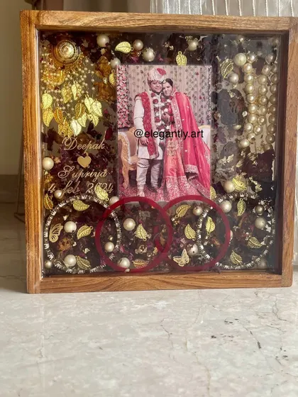 This teakwood frame is a treasure chest of memories, preserving wedding garlands, kaleera, and bangles alongside the couple's photo. The red bangles add a beautiful pop of color.