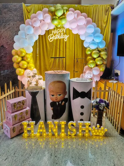 A stylish Boss Baby theme for Hanish, featuring custom-printed pedestals with a suit and tie design, a golden curtain backdrop, and marquee letters spelling out his name.