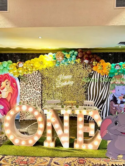 A complete jungle theme setup for a first birthday. It features a "ONE" table, a personalized photo frame, and various animal cutouts against a multi-patterned backdrop.